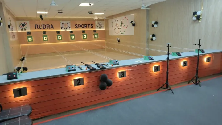 The firing line with six numbered lanes, air rifles on the counter and the Rudra Sports target wall behind